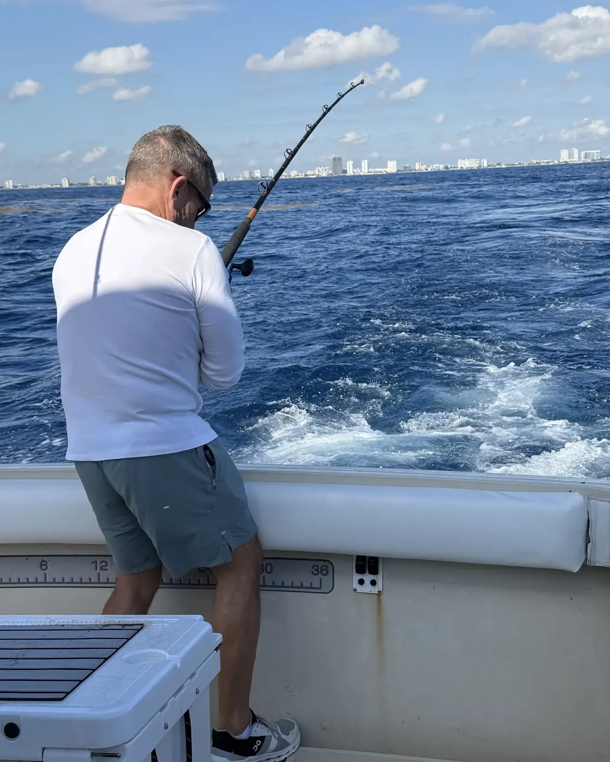 An angler leaning into a bent rod with the Pompano Beach skyline behind the boat
