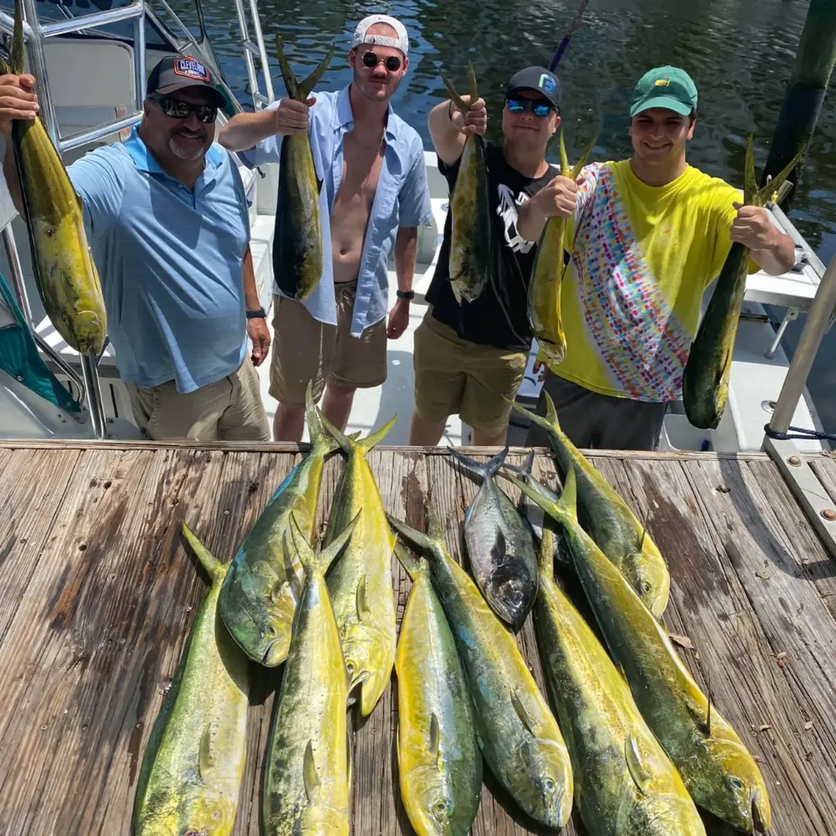 Two children in life jackets holding up a kingfish with the captain on the back deck