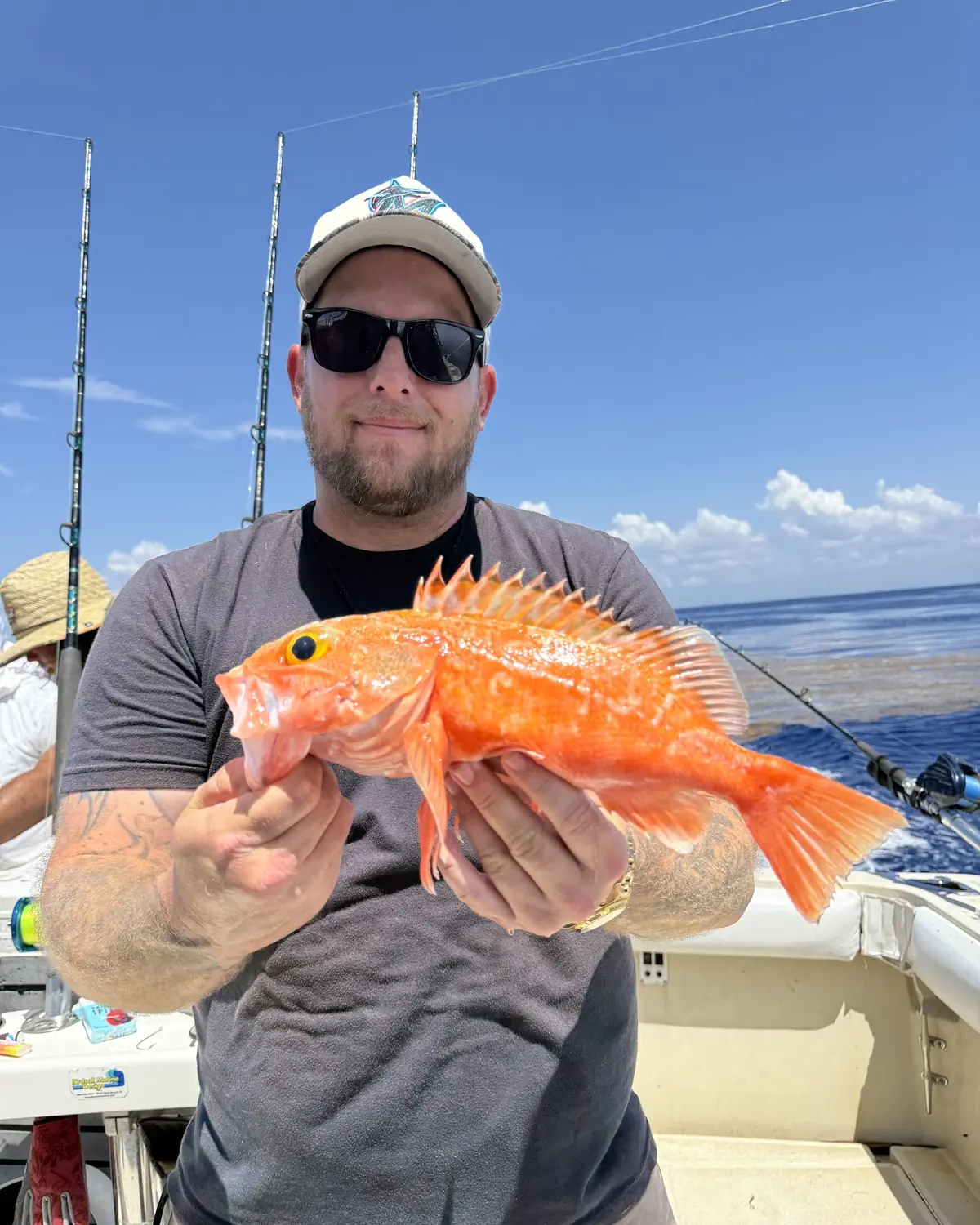 An angler holding a bright orange deep-water snapper on the back deck